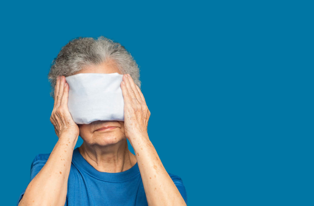 A senior woman is covering her eyes with a warm towel to treat her dry eyes.