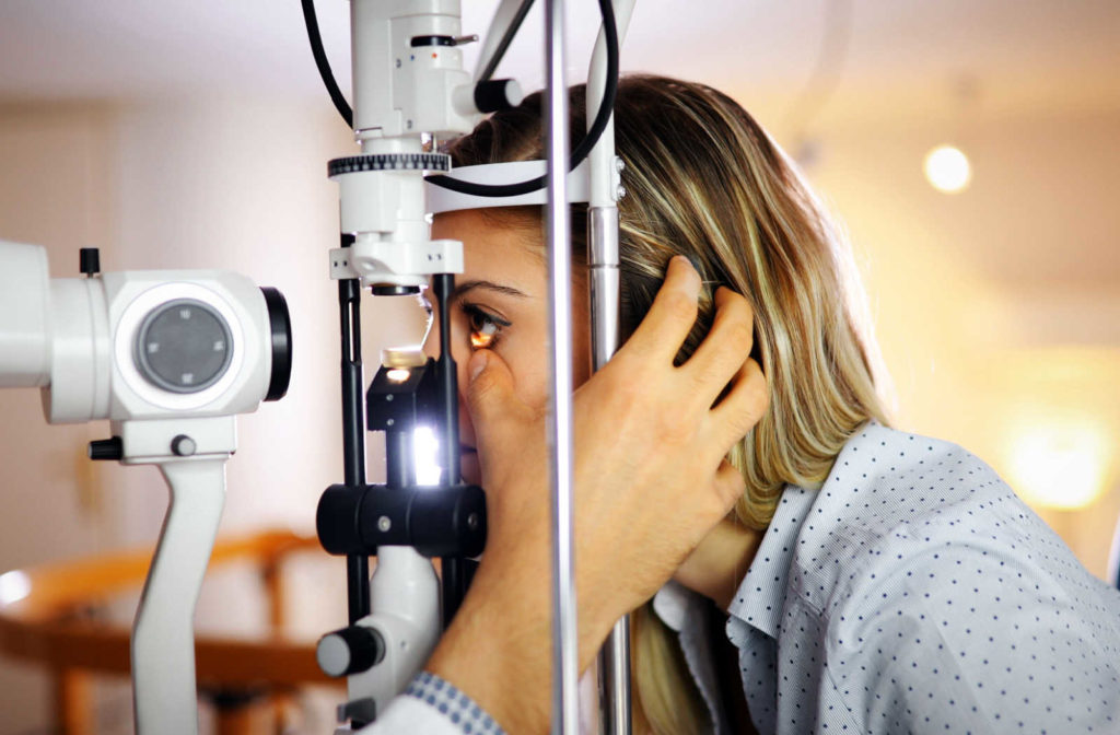 A patient sitting in front of a slit lamp and an eye care professional examining the health condition of her eyes.