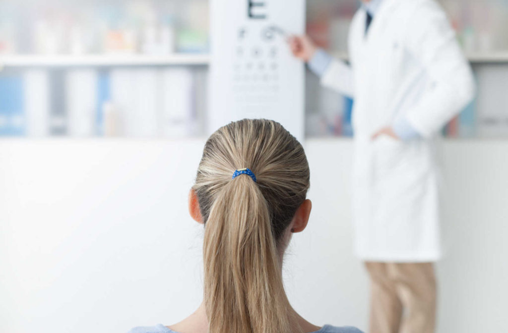 A young woman taking an acuity test and a male optometrist pointing to a spot on a Snellen chart.