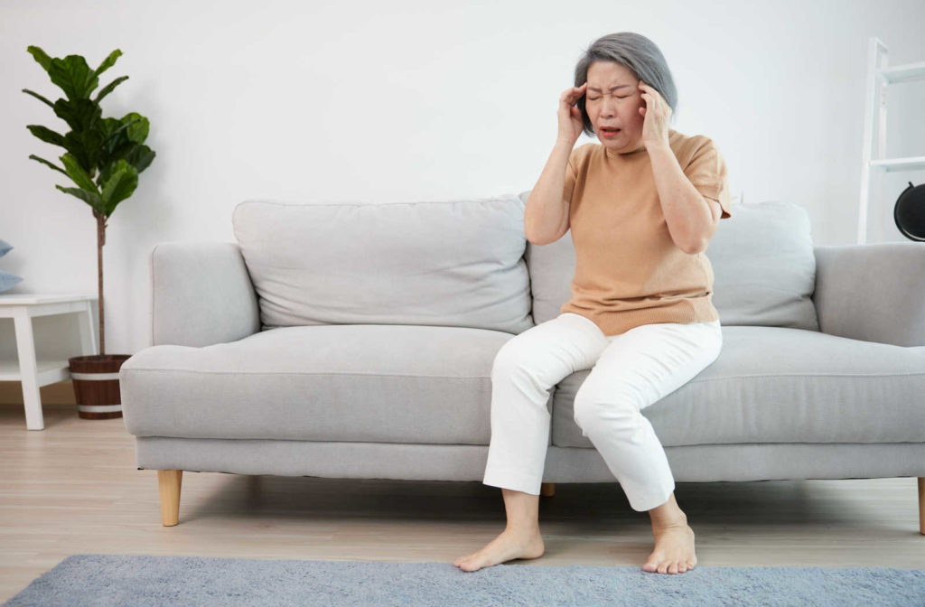 A senior woman on a couch suffering from a headache which is a sign of glaucoma.