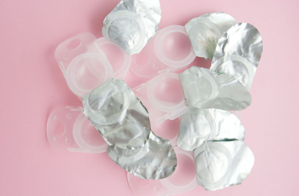 Open packets of daily disposable contact lenses in a pile on a pink background.