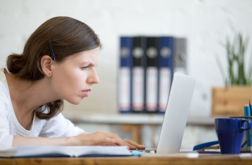 A woman typing on her laptop and leaning in close to read the screen, showing signs of nearsightedness.
