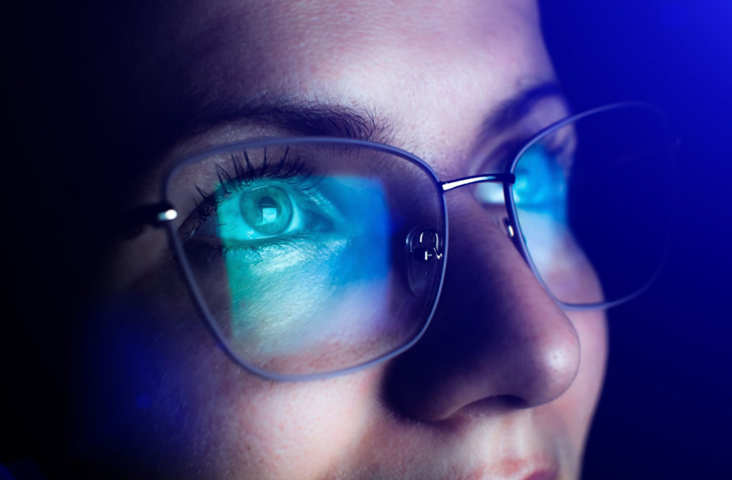 Close-up of woman with blue light reflected on her glasses from a screen.