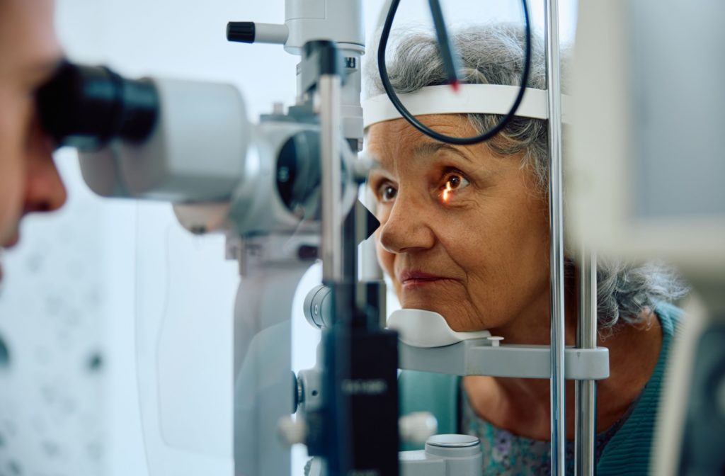 An older adult's eyes are being examined by an optometrist using a slit lamp.