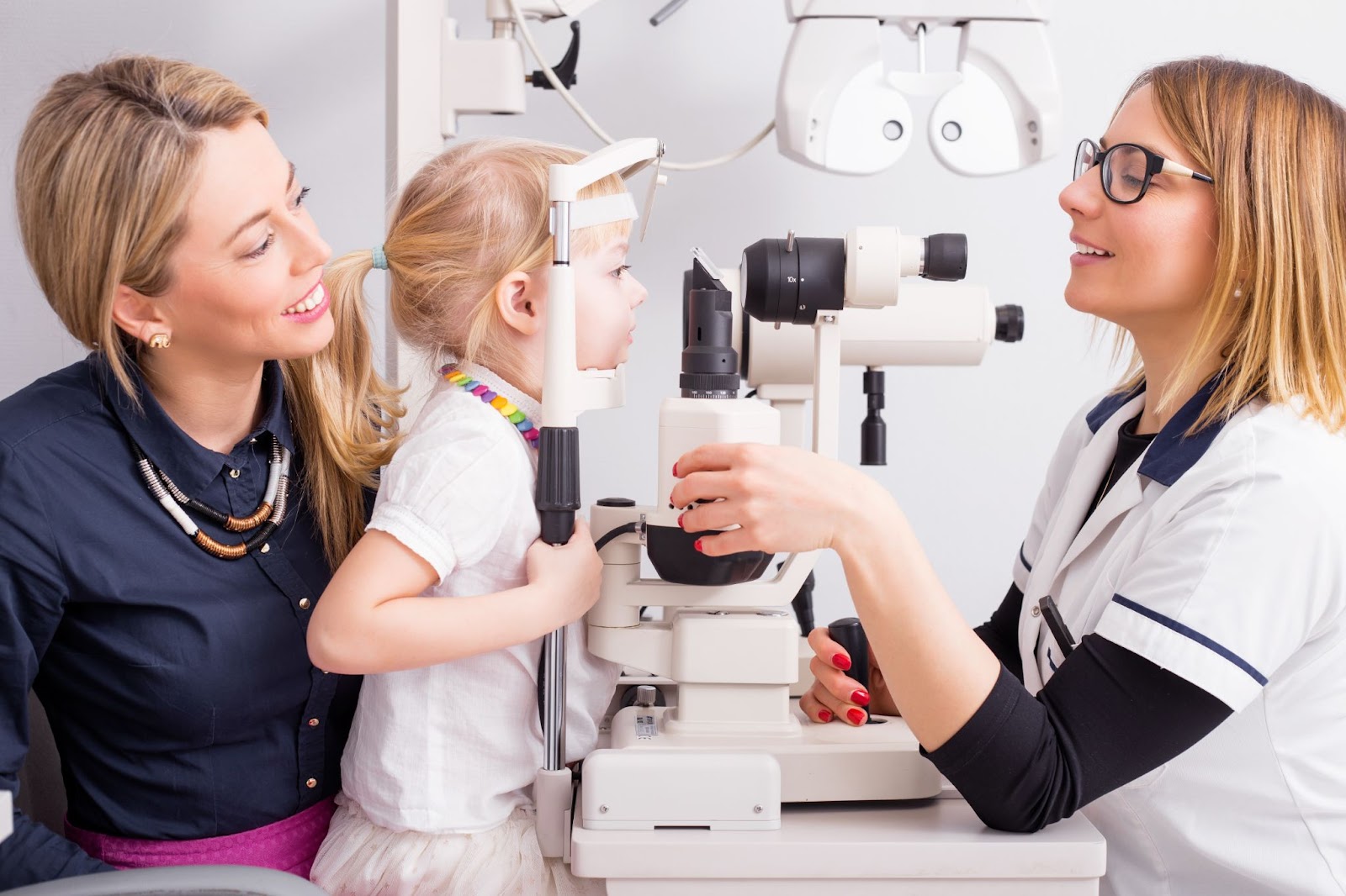 A young girl on her mom’s lap looks through a machine so her optometrist can check her vision health.