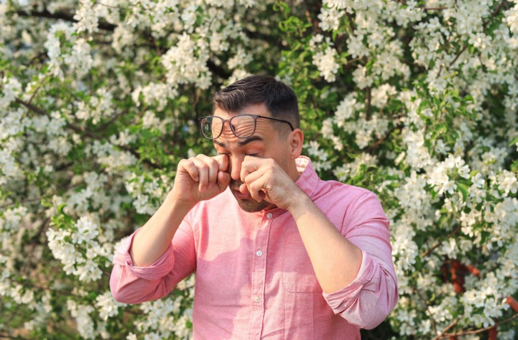 A man standing outside wipes his watery eyes, irritated by seasonal allergies.