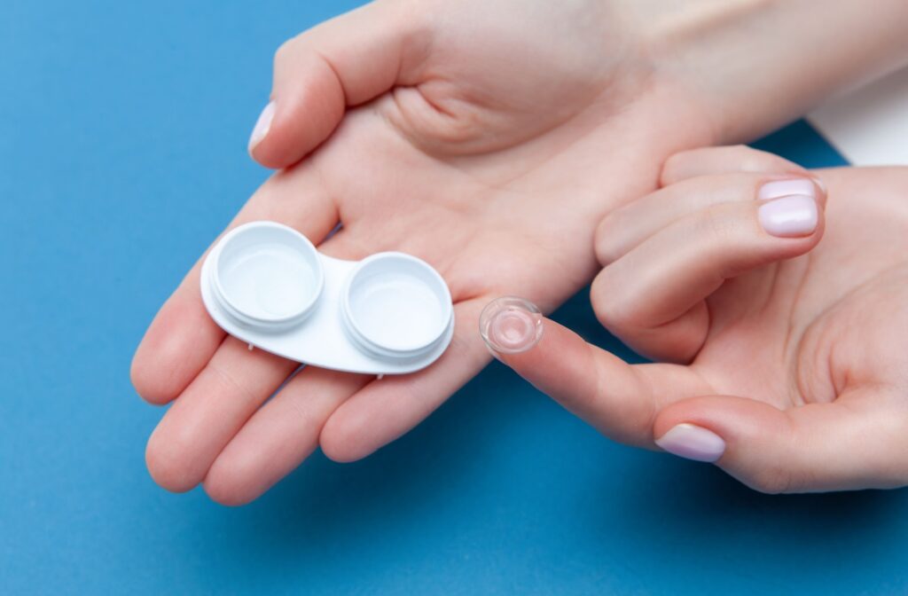 A person holding a contact lens on the tip of one finger with a white case in their hands.