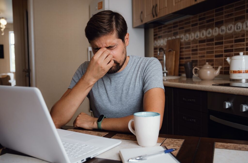 A man rubs his eye in discomfort while drinking coffee.