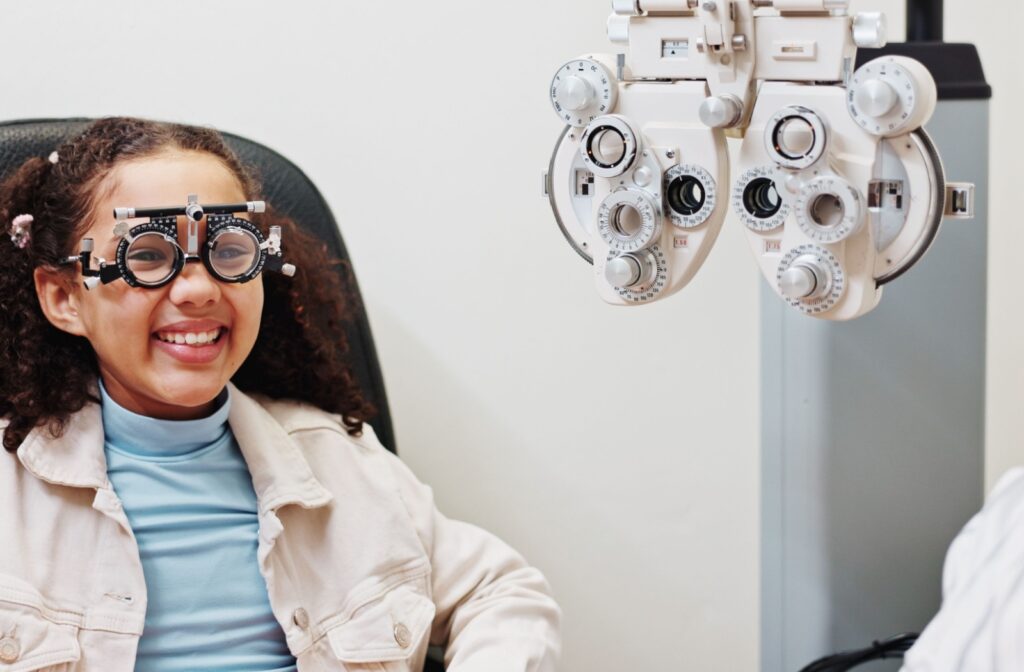 A young optometry patient wearing phoropter lenses and laughing during their eye exam.