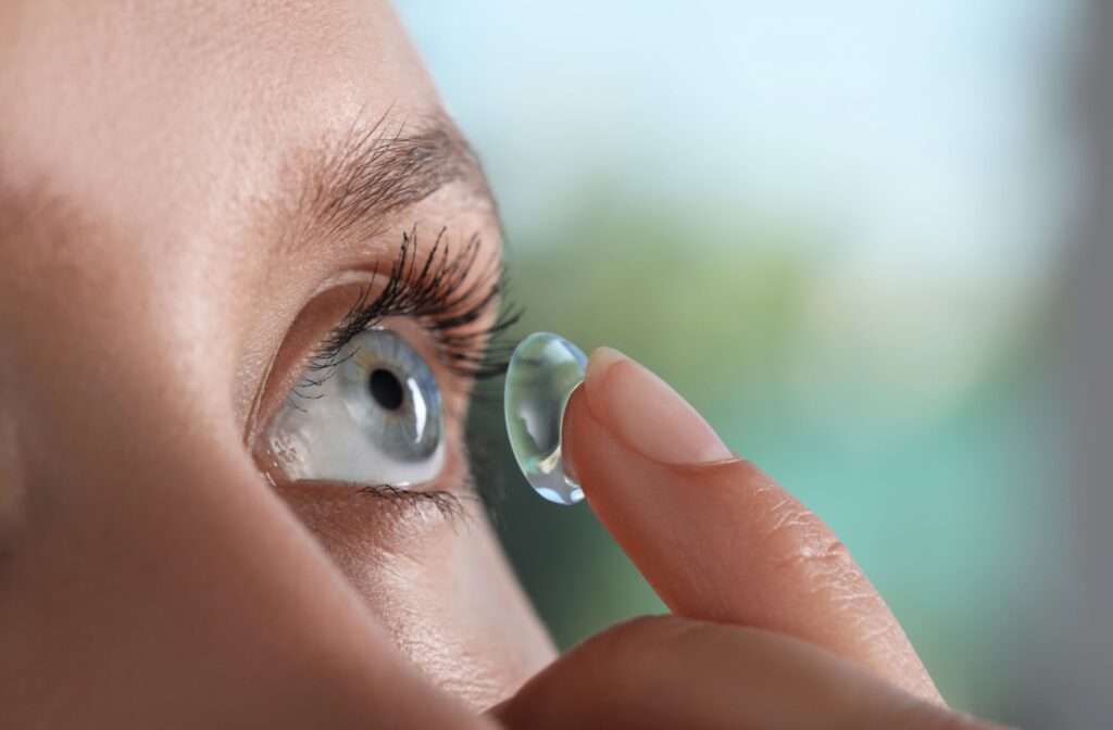 A close-up image of a person inserting a contact lens to help with their dry eyes.