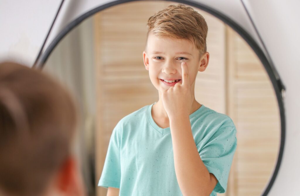 Young smiling boy putting in contact lenses in front of a large rough mirror.