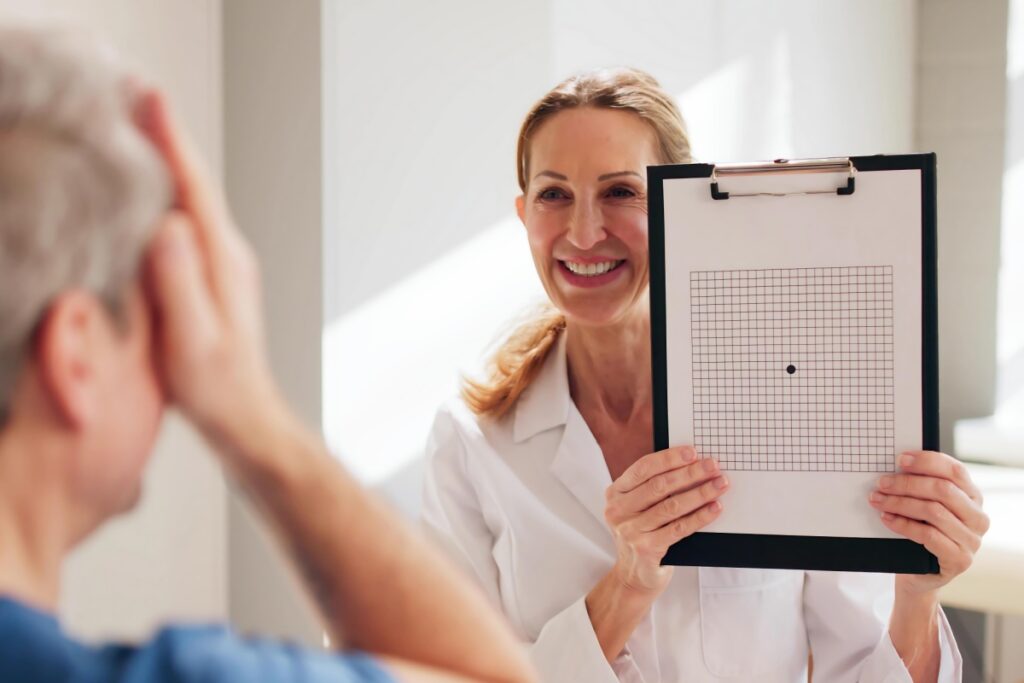 Smiling female eye doctor in white coat holding vision chart while conducting eye examination with patient in clinical setting.