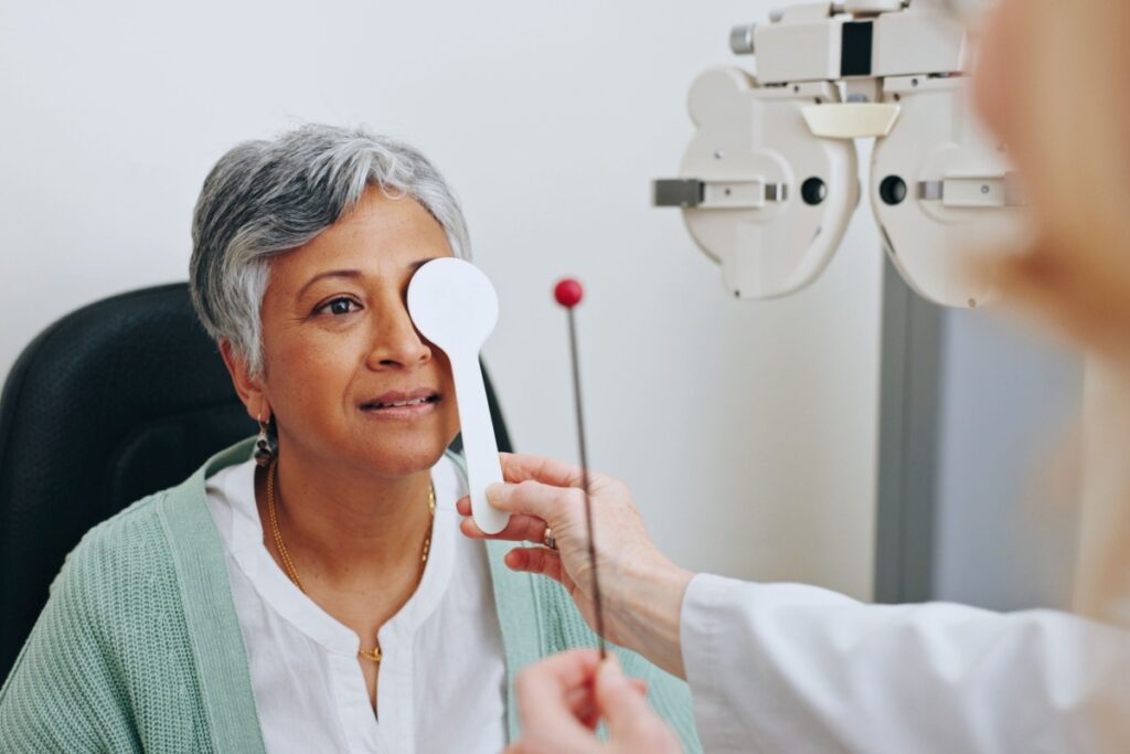 Optometrist conducting a cover test on an older woman during a comprehensive eye exam to assess eye muscle alignment and focus coordination.