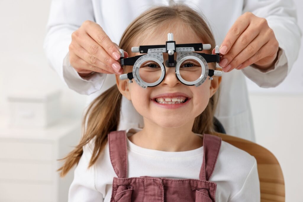 Optometrist adjusting trial frames on smiling young girl during comprehensive eye examination in office.