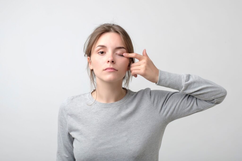 Woman pointing to her eye indicating eye irritation, discomfort, or potential contact lens-related issue.